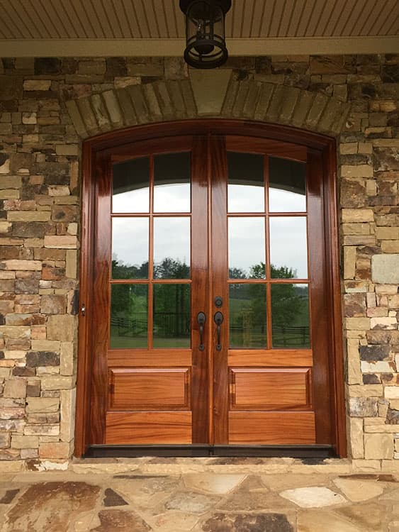 House plan exterior featuring arched stone surround above double wood doors with divided light windows and rustic stone exterior.