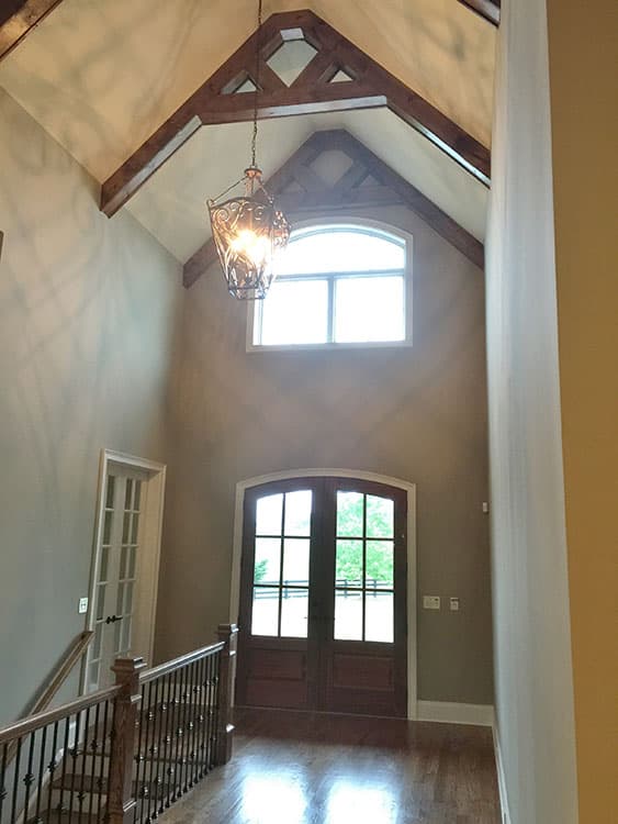 Interior view of foyer with vaulted ceiling, exposed wood beams, arched double doors, and a decorative chandelier.