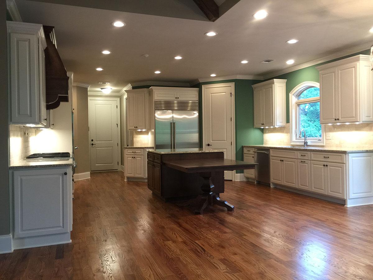 Spacious kitchen featuring white cabinetry, a central dark wood island, stainless steel refrigerator, and a bay window over the sink.