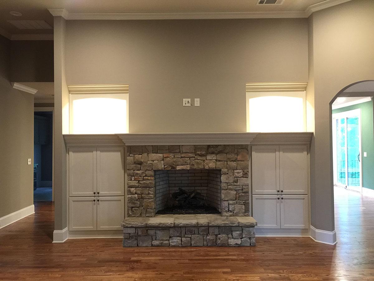Living room with stone fireplace, built-in cabinets, and arched doorway to another room.
