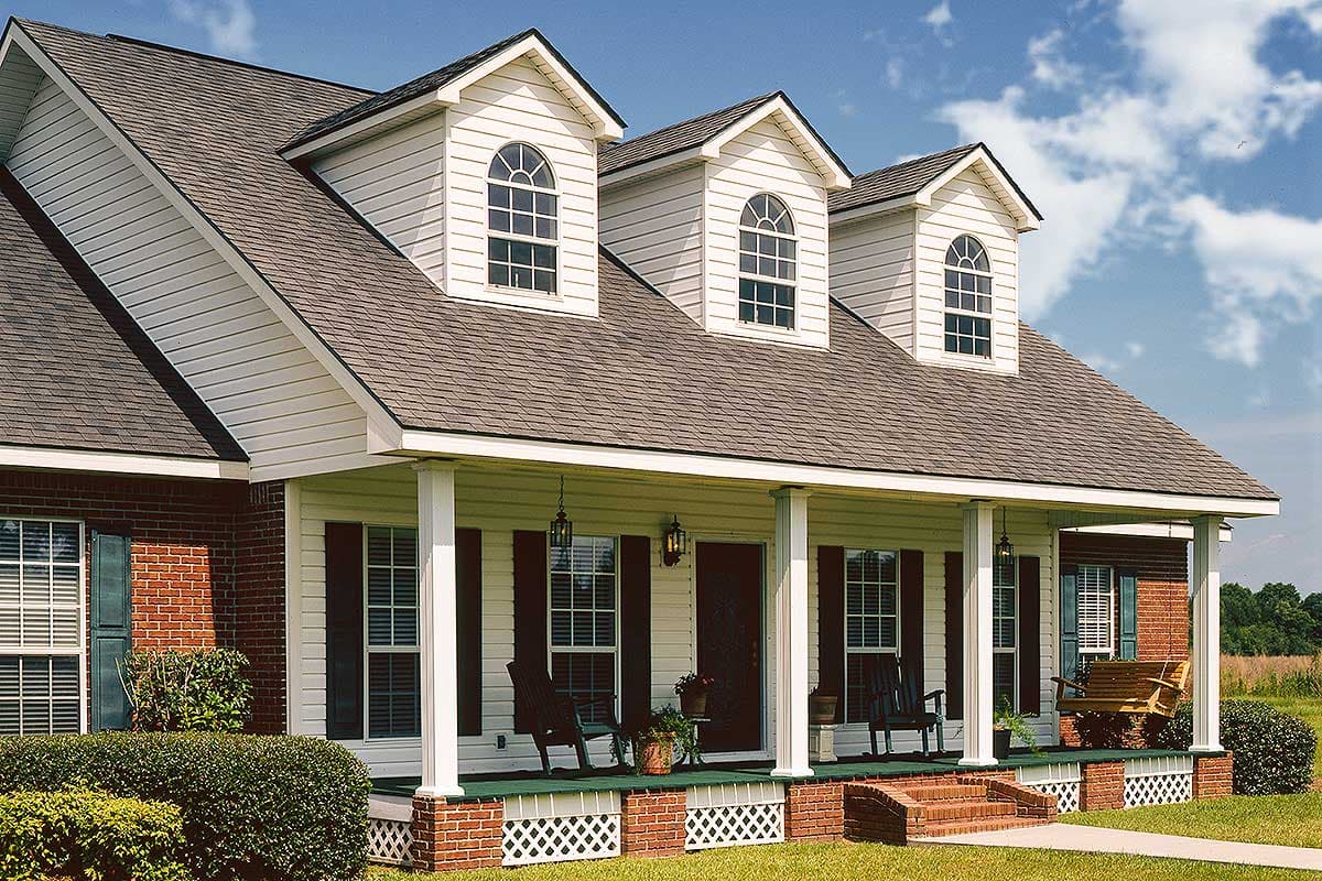 House plan exterior: Traditional two-story home with a full-width covered porch, brick accents, and three dormer windows with arched tops.
