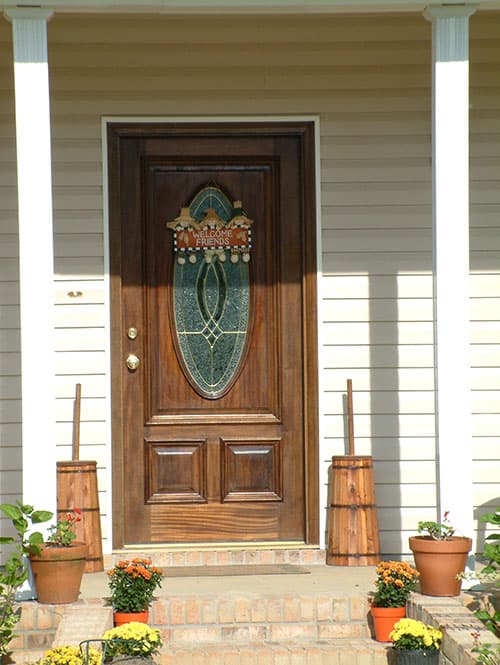 House plan exterior: wooden front door with oval stained glass, covered porch with two white columns, clapboard siding.