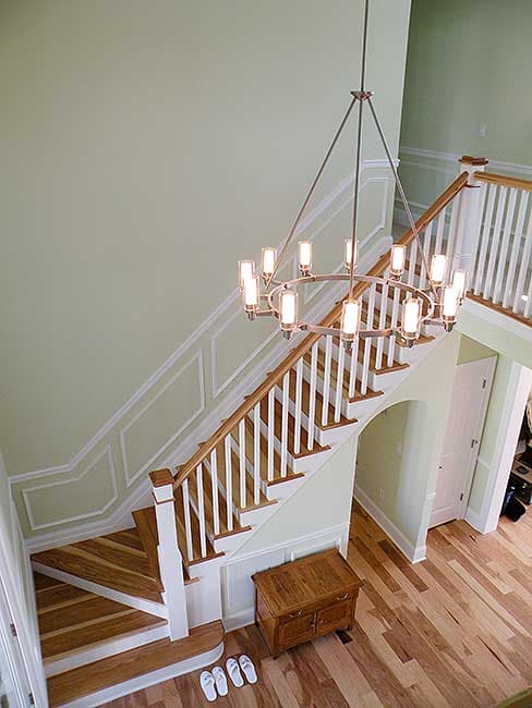 Interior view of staircase with wood treads, white risers, wainscoting, and a modern chandelier.