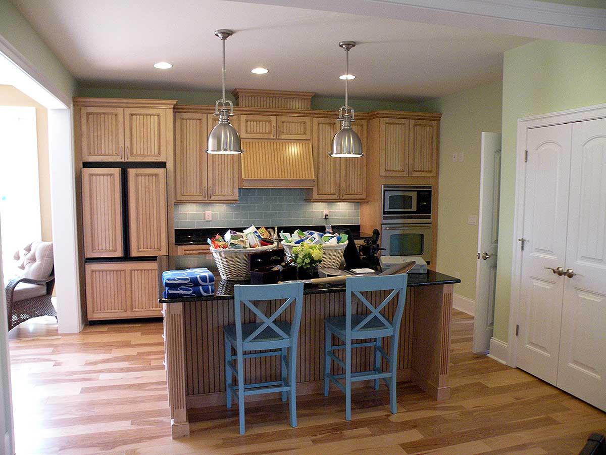 Kitchen with light wood cabinetry, black granite island with blue stools, and stainless steel appliances.