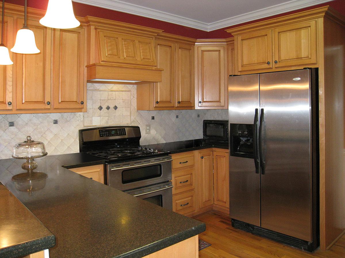 Kitchen featuring light wood cabinets, stainless steel appliances including a double-door refrigerator and gas range, and dark granite countertops.