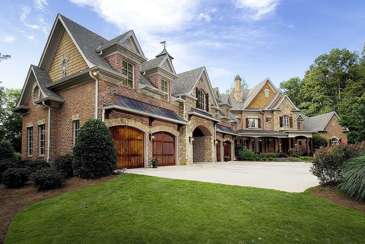 House plan exterior: Tudor style, multi-story brick home with arched wooden garage doors, stone accents, and complex rooflines.