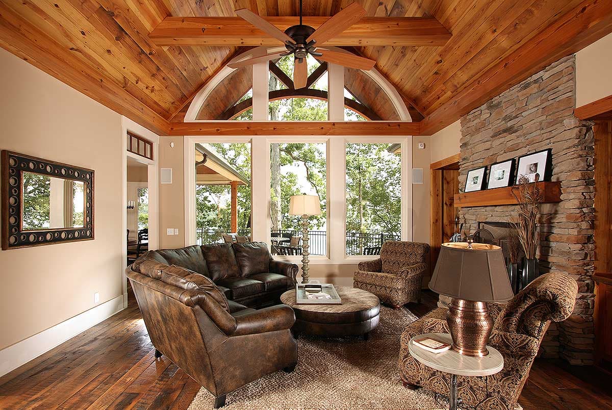 Living room with vaulted wood ceiling, stone fireplace, large windows, and leather seating.