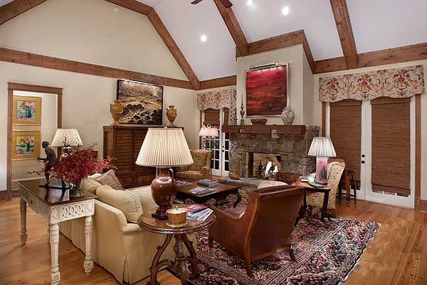 Living room with vaulted ceiling, exposed beams, stone fireplace, and large windows.