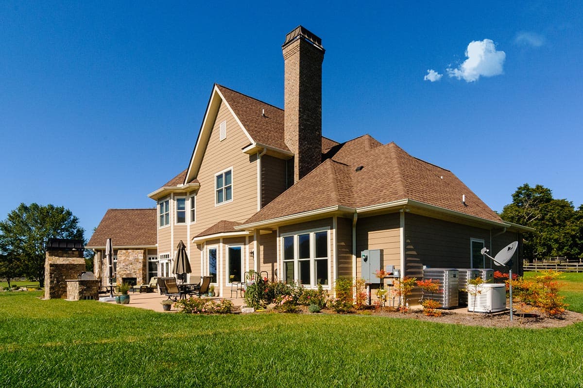 House plan exterior featuring a tan siding, brick chimney, multi-level roof, and patio with outdoor kitchen.