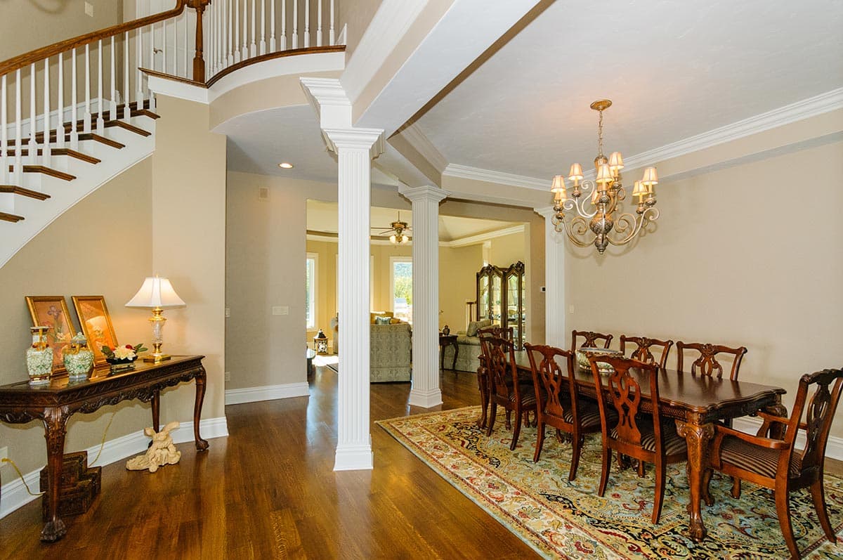 Interior view of dining room with ornate chandelier, table, chairs, and view into adjacent living area with staircase.
