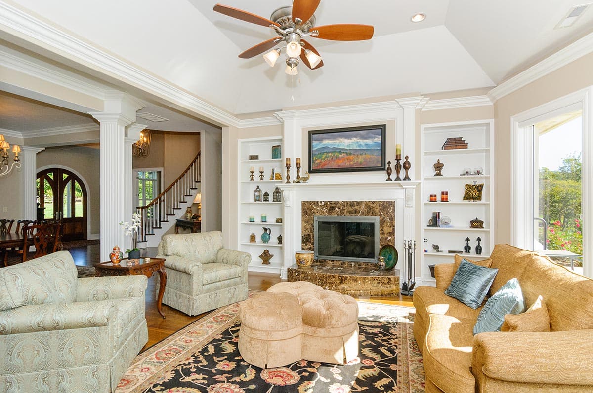 Living room with fireplace, built-in shelving, a ceiling fan, and an adjacent dining area with arched double doors.