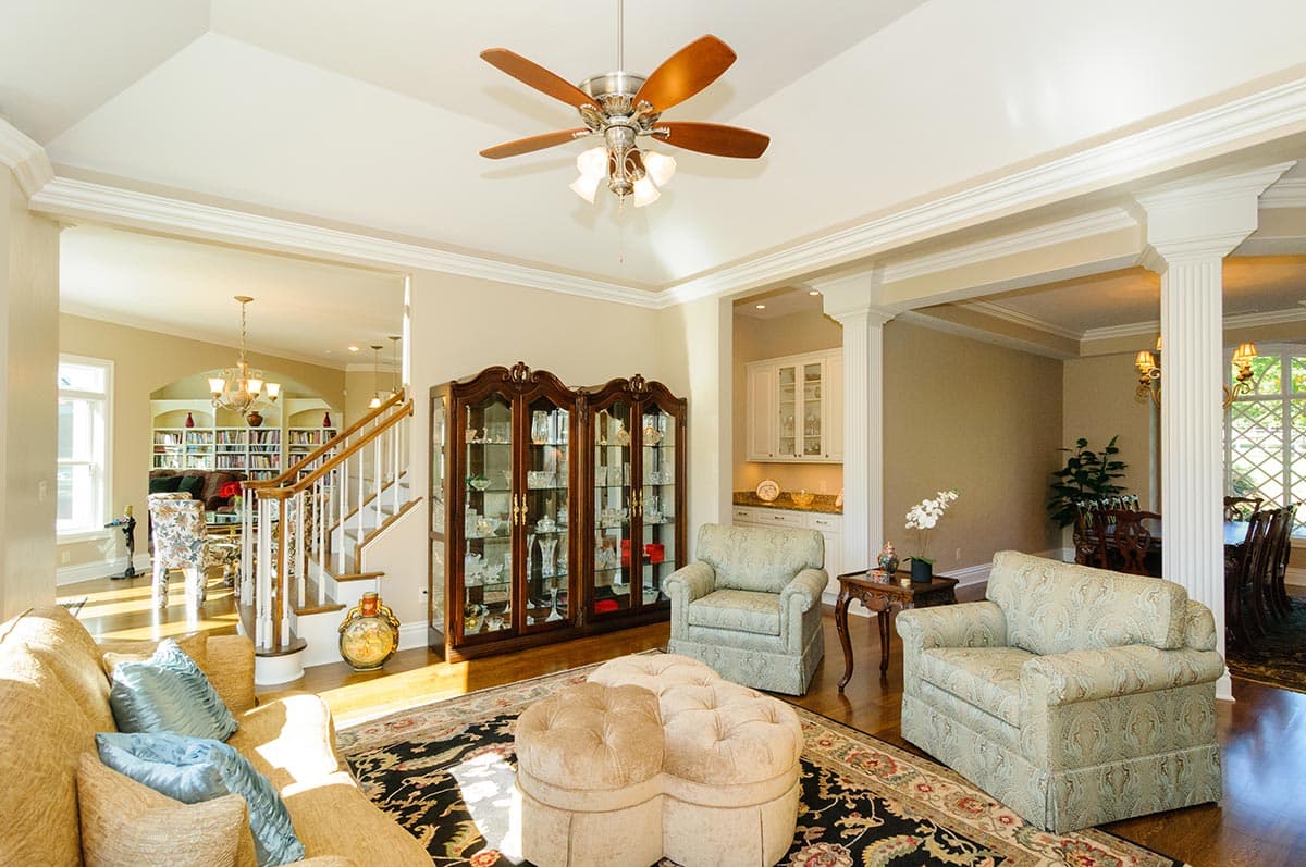 Interior view of a living room with a fireplace, built-in bookshelves, and a staircase. Vaulted ceiling with fan.