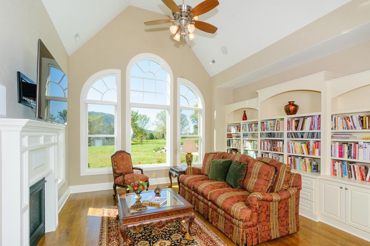 Interior view of a living room with vaulted ceiling, fireplace, built-in bookshelves, and arched windows.
