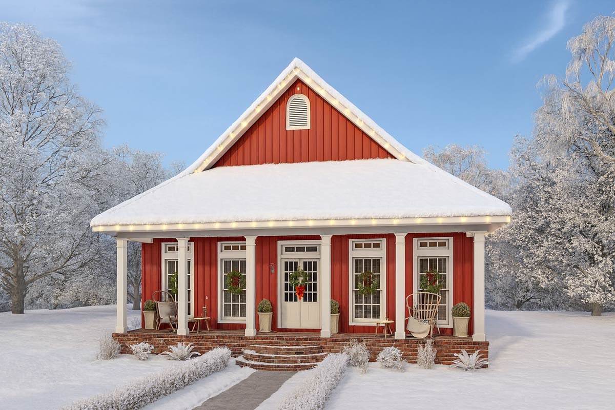A charming red house is covered in snow, with holiday wreaths and lights. It's nestled in a winter landscape with frosted trees and a clear blue sky.