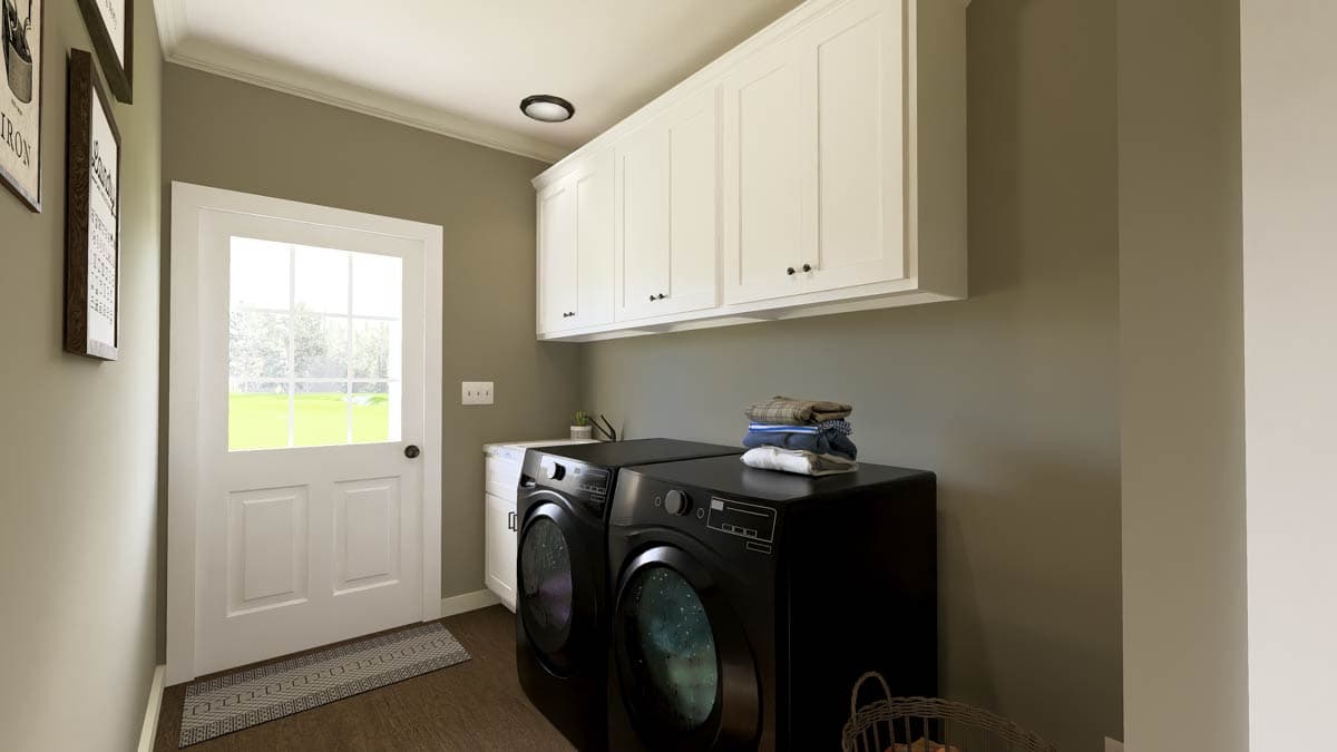 A laundry room with black washer and dryer units. White cabinets are above, with a door and window to the left. A folded stack of clothes sits on top.