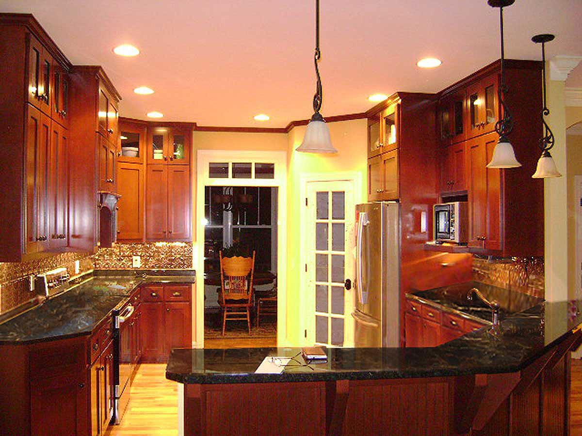 Interior view of a kitchen with dark wood cabinets, granite countertops, stainless steel refrigerator, and pendant lighting.