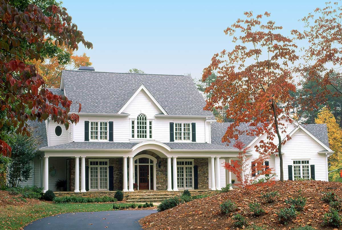House plan exterior: White two-story home with stone accents, wraparound porch with columns, and arched entryway.