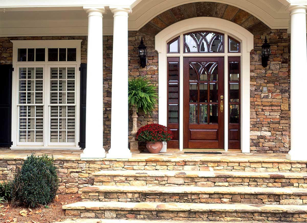 House plan exterior: Stone facade, arched entry with glass door, columns, and multi-pane windows.