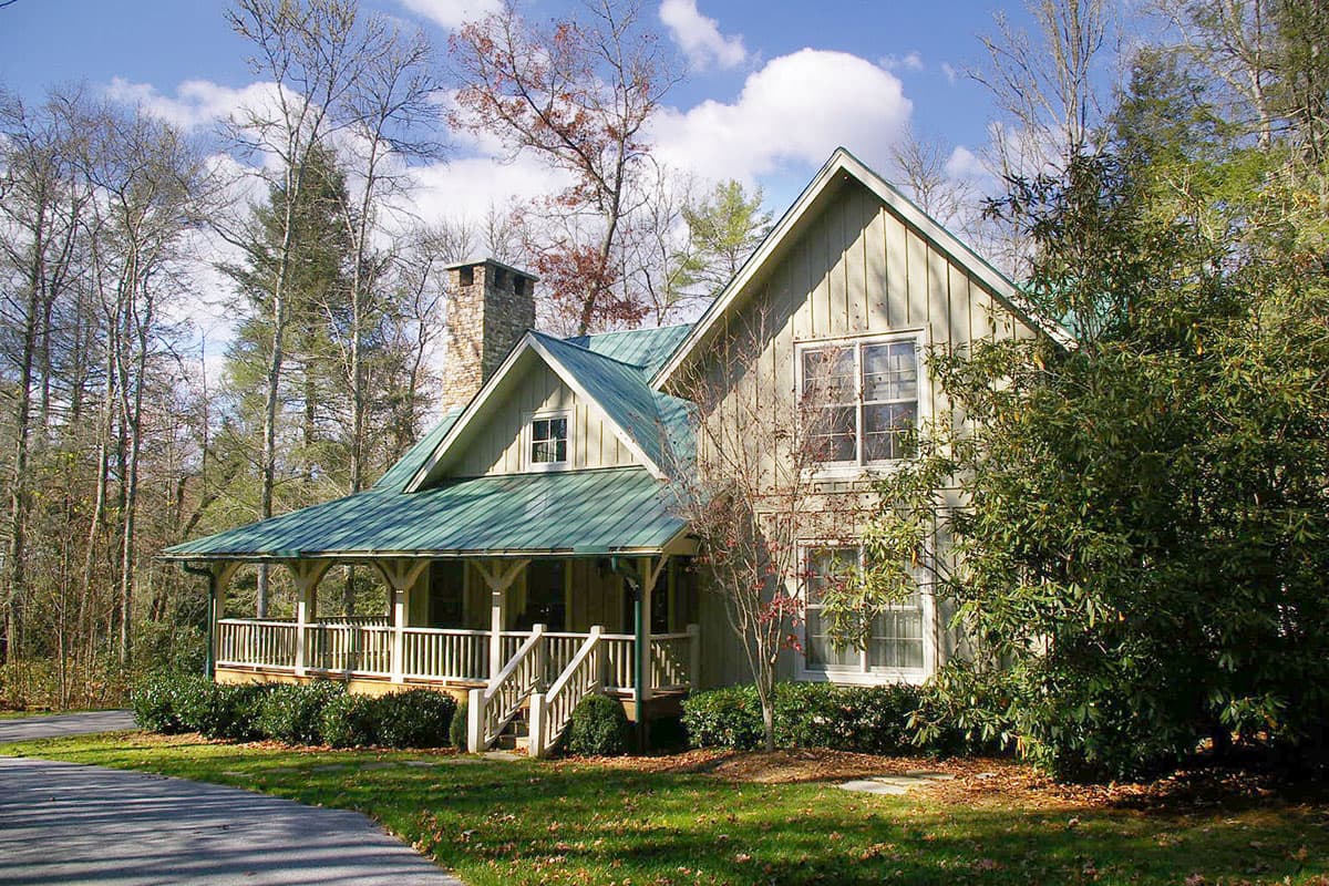 House plan exterior: Two-story Craftsman style home with a wraparound porch, stone chimney, and green metal roof.