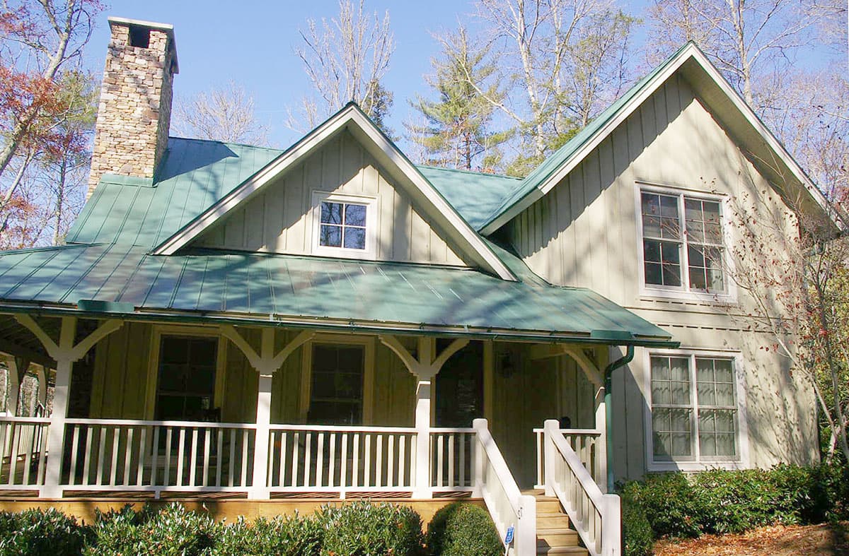 Craftsman house plan exterior with green metal roof, stone chimney, and wraparound porch with white railings.