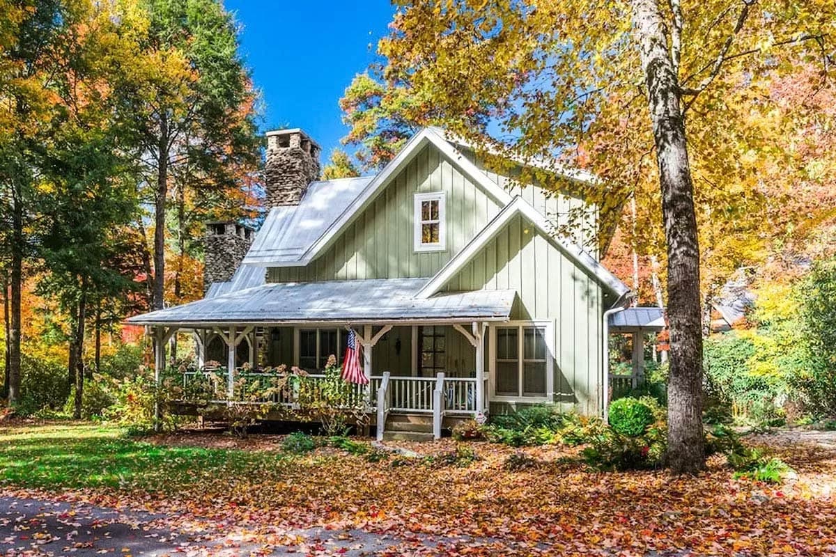 House plan exterior of a two-story cottage with a wrap-around porch, stone chimney, and metal roof.