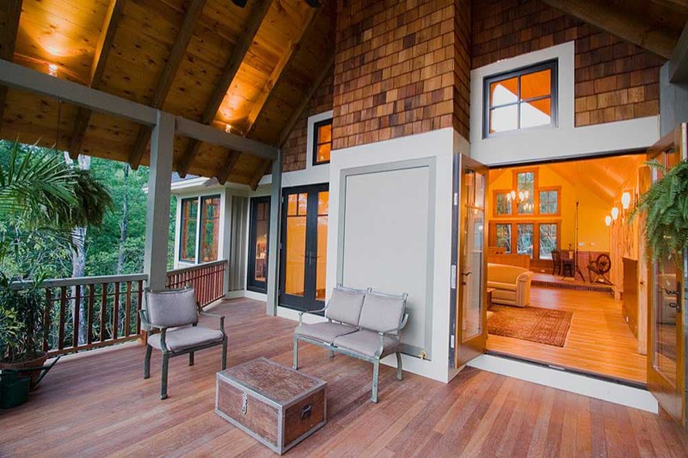 Covered porch with wood ceiling and cedar shingle chimney, opening into a great room with vaulted ceiling and large windows.