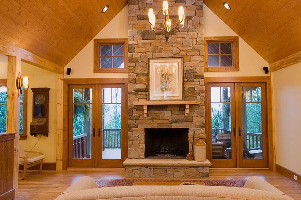 Great room with vaulted wood ceiling, stone fireplace, and double glass doors opening to a porch.
