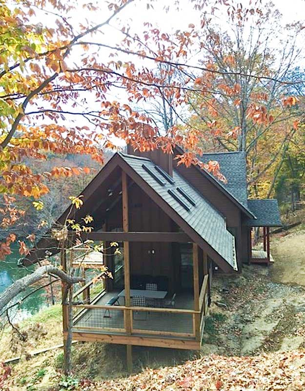 House plan exterior: two-story cabin with covered porch, gable roof, and dormer windows.