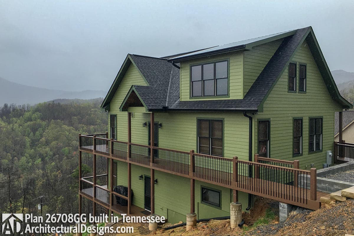 House plan exterior with two stories, green siding, multiple gables, and a wraparound deck.