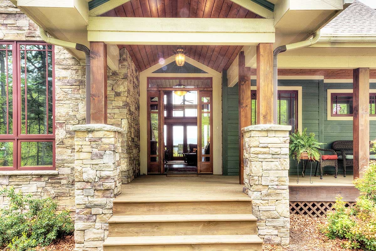 House plan exterior: wood-clad porch with stone pillars, large windows, and double front doors.