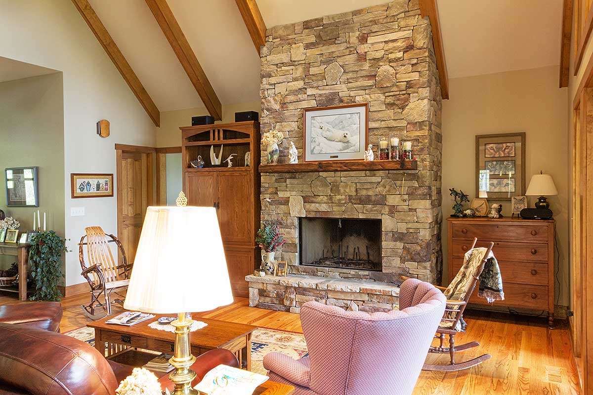 Living room interior with vaulted wood-beamed ceiling, large stone fireplace, and wood cabinetry.