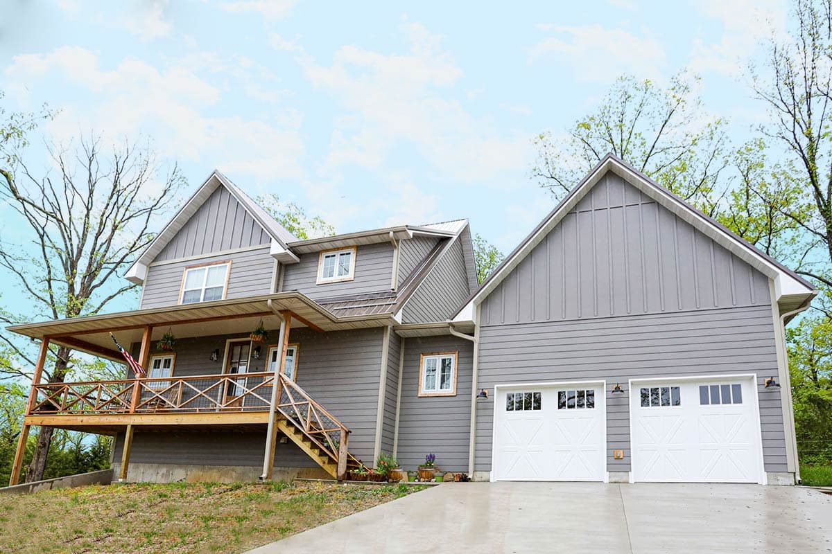 House plan exterior with two stories, a front porch with railing, and a gabled roof. Attached garage features two overhead doors.