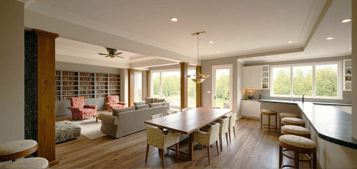 Open concept living area with built-in bookshelves, dining table, kitchen island with seating, and large windows.