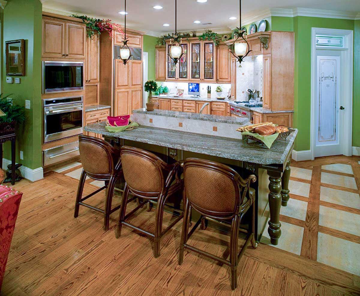 Kitchen with wood cabinetry, large island with seating, stainless steel appliances, and a pantry door.