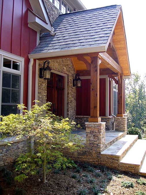 House plan exterior: Rustic porch with stone base, timber posts, and stone steps. Wood siding and dormer window visible.