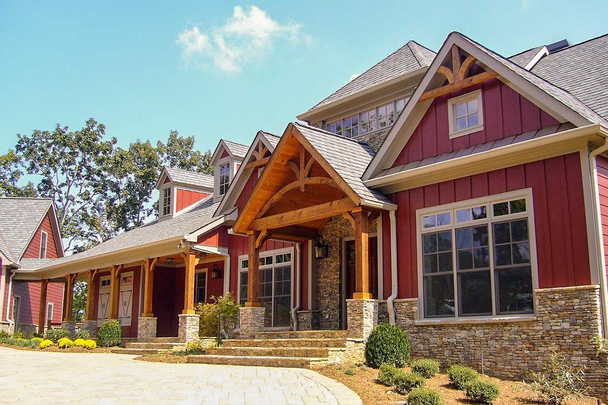 House plan exterior: Two-story home with stone accents, prominent gables, dormer windows, and a covered entry with exposed timber framing.