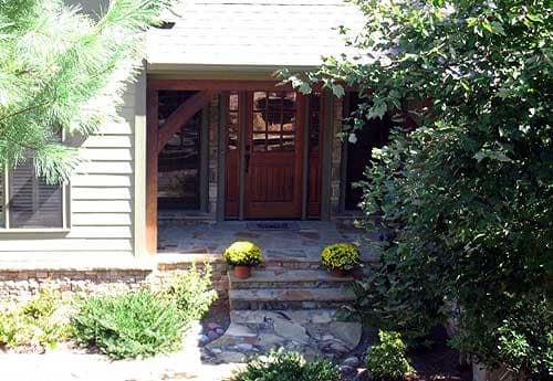 House plan exterior: Covered entry with wood double doors, stone steps, timber supports, clapboard siding, and gable roof.