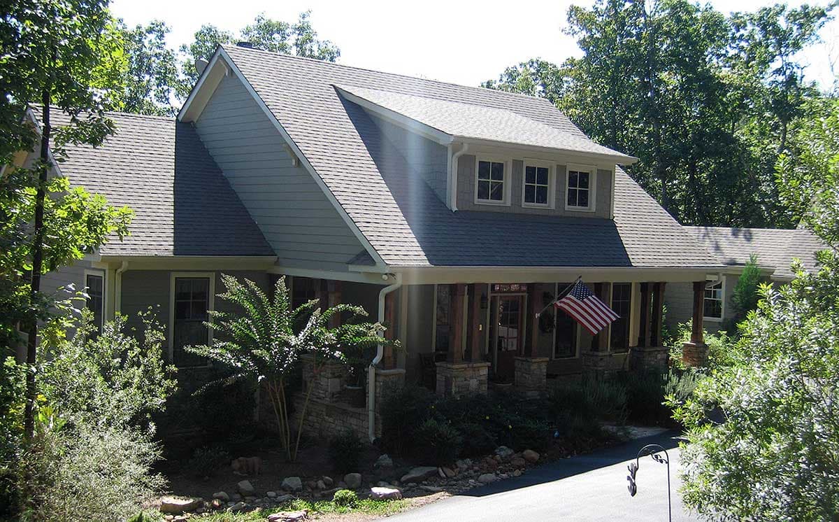 House plan exterior with hipped roof, dormer windows, covered porch with stone columns, and double-hung windows.