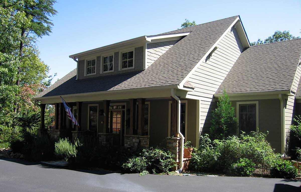 House plan exterior with prominent gables, dormer windows, and a covered porch supported by stone and wood columns.