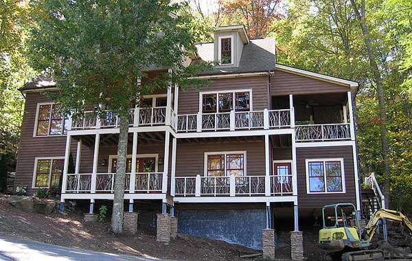 House plan exterior: Three-story home with multiple decks, dormer window, and stacked stone foundation.