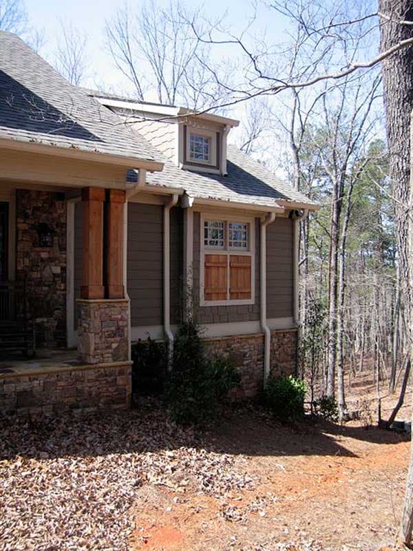 House plan exterior with stone accents, gabled dormer, wood shutters, and timber porch columns.