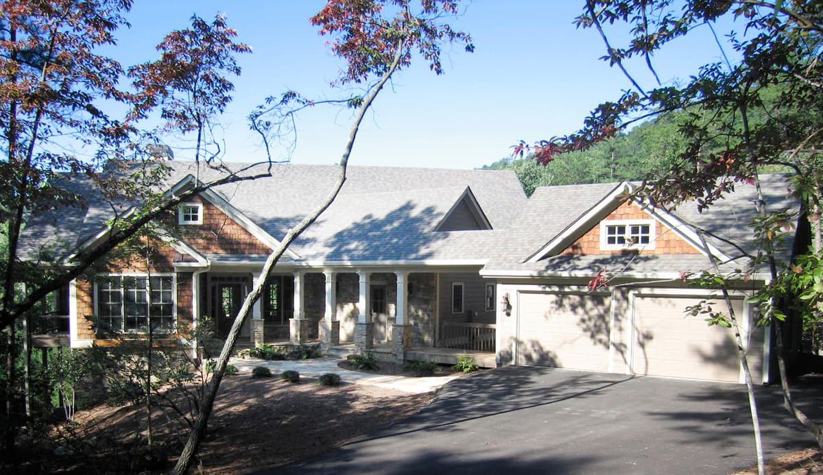 House plan exterior with a covered porch, stone accents, gable dormers, and a side-entry three-car garage.