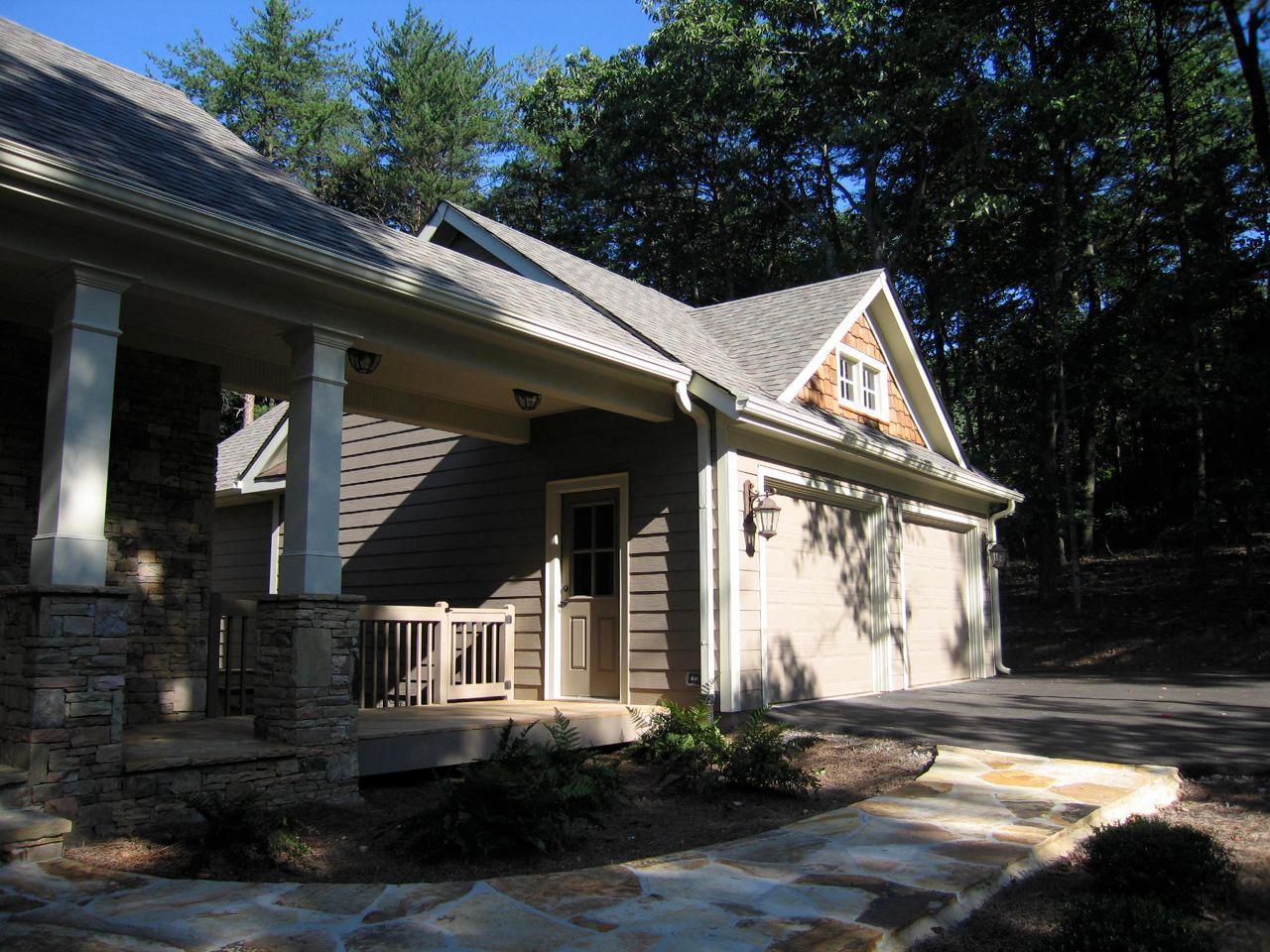 House plan exterior showing a two-car garage, covered porch with stone columns, and a dormer window.