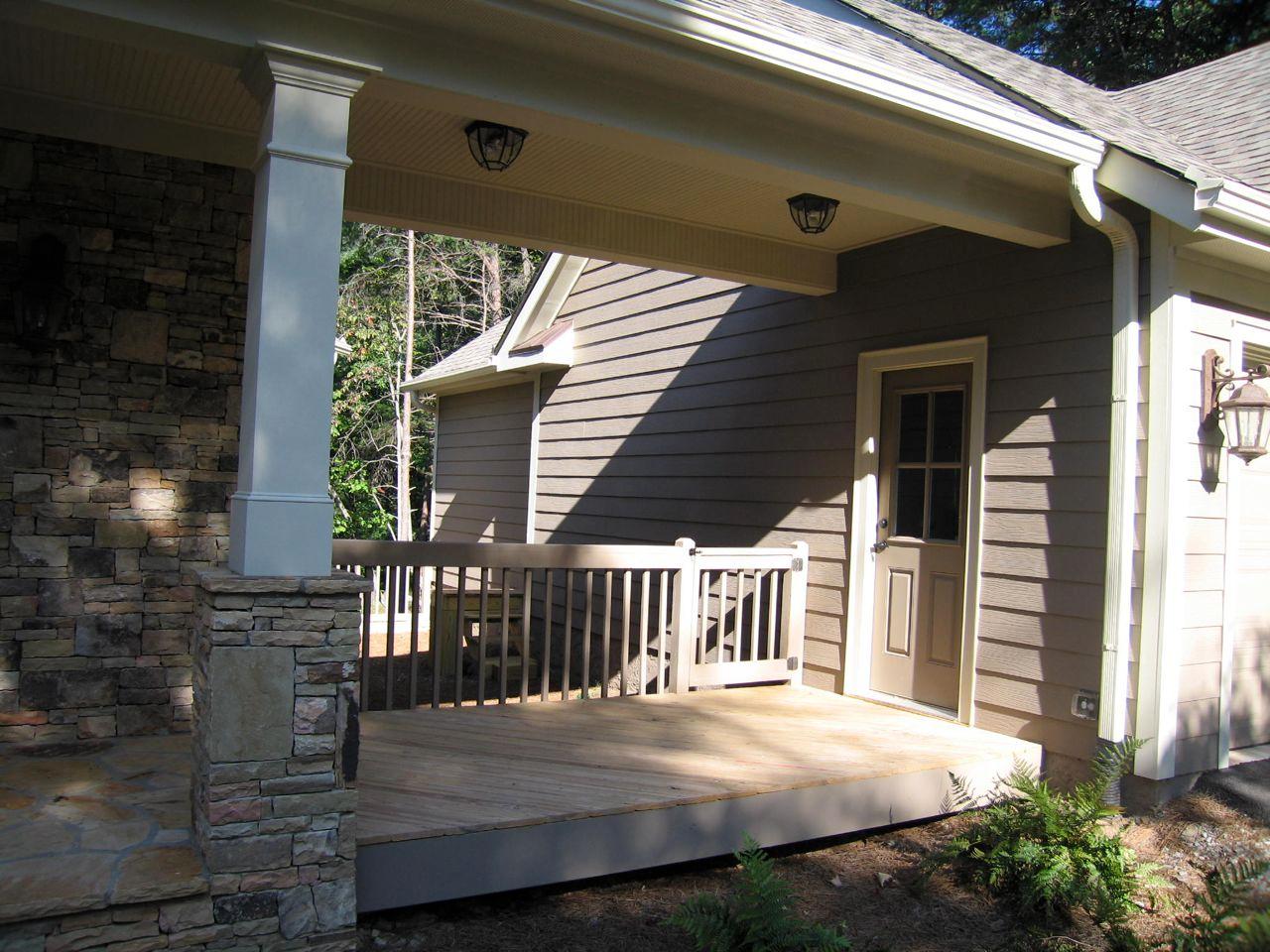 House plan exterior featuring a covered deck with stone pillar, tan siding, and a glass-paneled door.