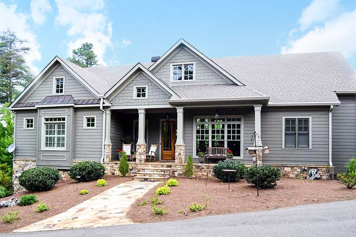 House plan exterior. Craftsman style with gabled roof, stone accents, and a covered porch supported by columns. Two story home with multiple windows.