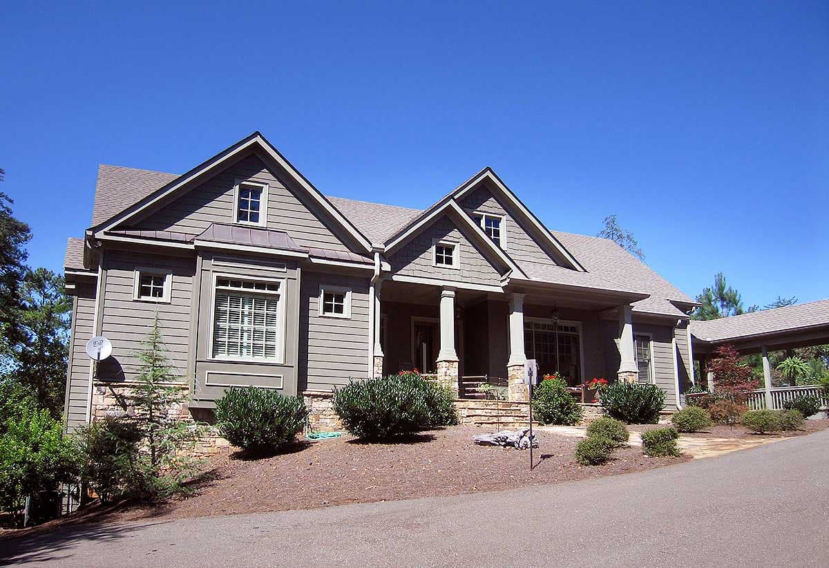 House plan exterior: Two-story home with horizontal siding, stone accents, gabled dormers, and a covered front porch with columns.