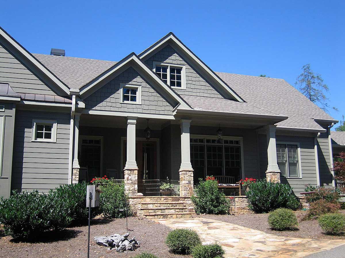 House plan exterior with gabled dormers, stone-clad porch supports, and horizontal siding. One and a half stories.
