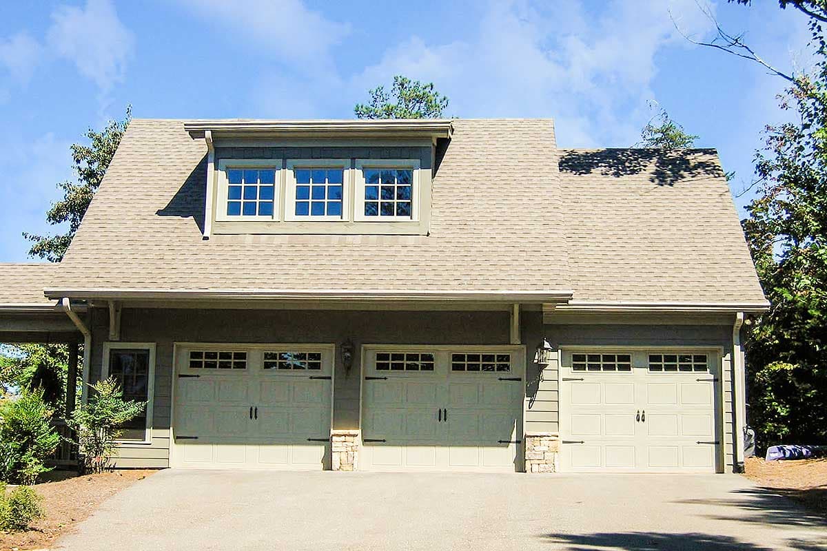House plan exterior with three garage bays, dormer windows with grid panes, and stone accents.