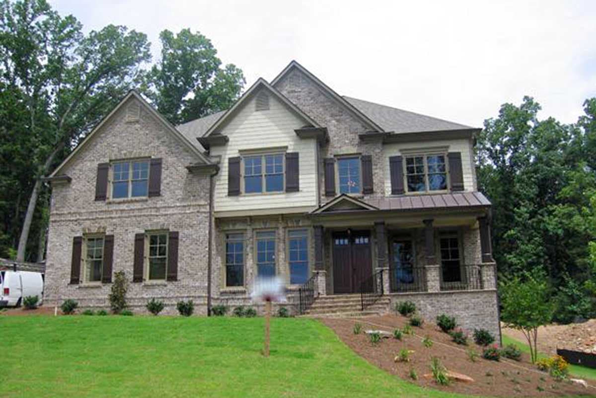 House plan exterior with two stories, brick facade, gabled roof, shuttered windows, and covered front porch with columns.