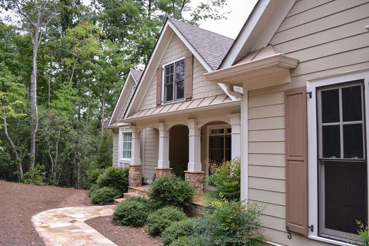 Craftsman style house plan exterior with a covered porch supported by stone-clad columns, gables, and dormers.